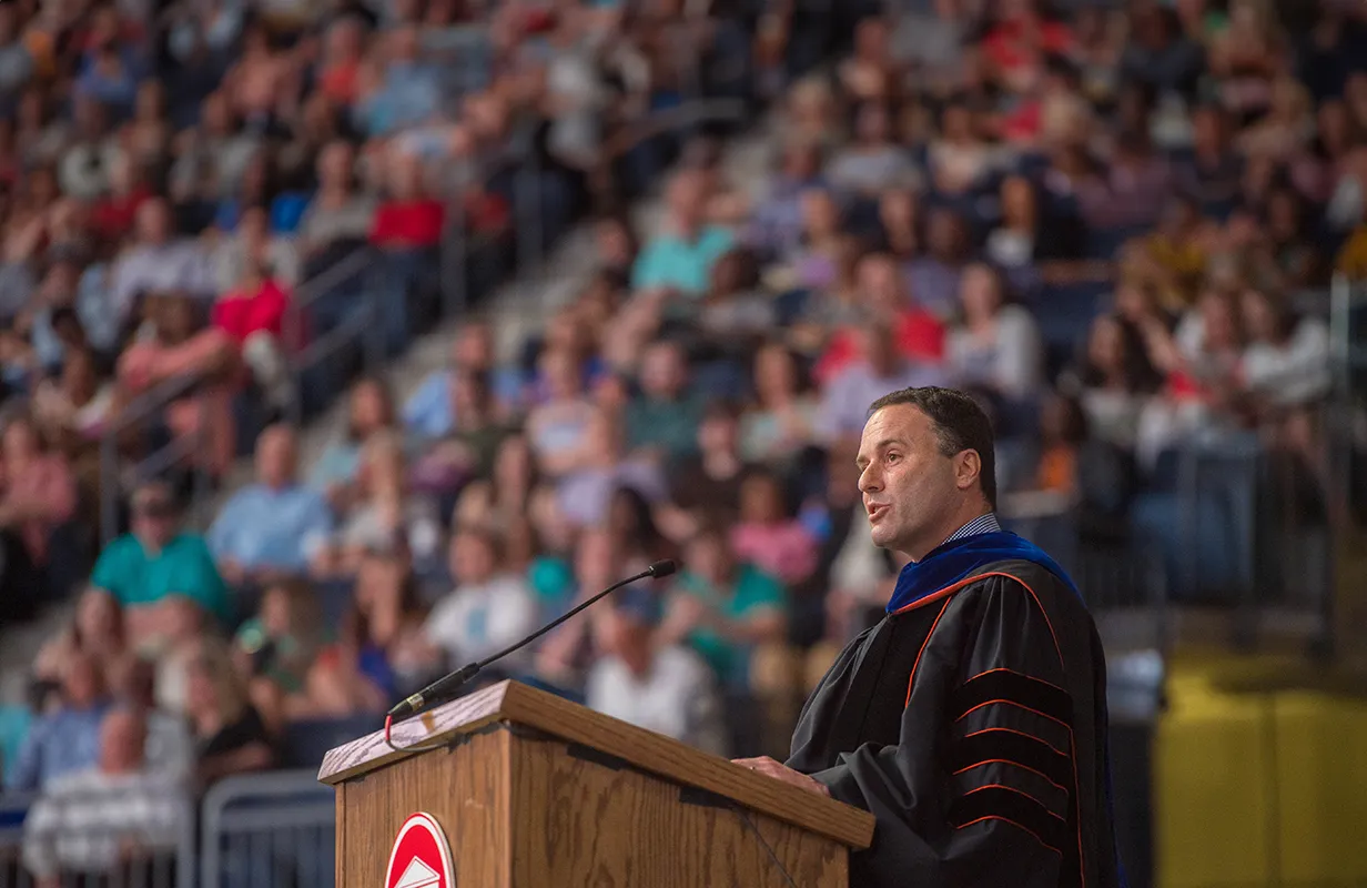 Dean Lee Cohen standing at podium in graduation regalia speaking to crowd