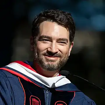 person in graduation regalia standing outdoors; smiling