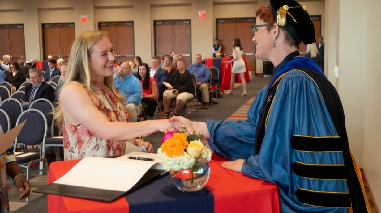 Phi Beta Kappa induction ceremony. student shaking the hand of a faculty member in graduation regalia