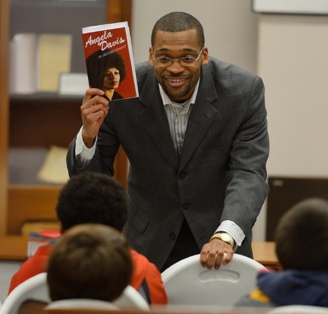 Dr. Patrick Alexander holding a book and smiling at a small audience seated in front of him