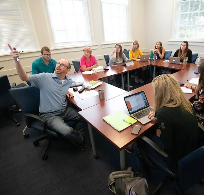 Professor pointing out of frame with eight students ringed around.