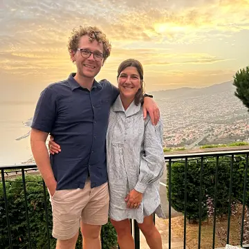 two people standing with arms around each other in front of a sunset
