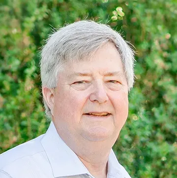 person smiling at camera standing in front of greenery