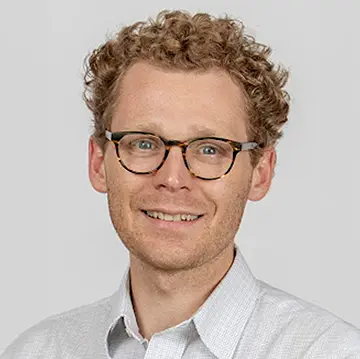 person in glasses with curly hair smiling; white background