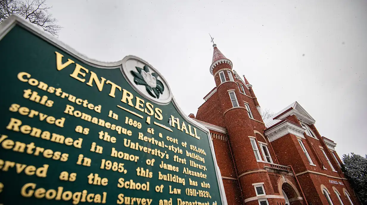 perspective of plaque in front of Ventress and Ventress Hall (red brick building with spires) in background. Tex on plaque reads: "VENTRESS HALL, constructed in 1889 at a cost of $35,000, this romanesque Revival-style building served as the University's first library. Renamed in honor of James Alexander Ventress in 1985, this building has also served as the School of Law (1911-1929) 