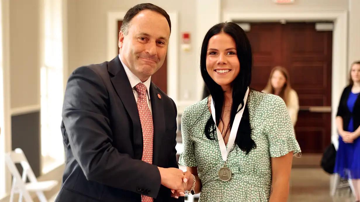 Dean of the College of Liberal Arts shakes hands with a student wearing a medal