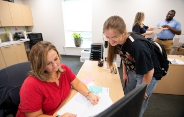 staff member helping a student with paperwork at her desk