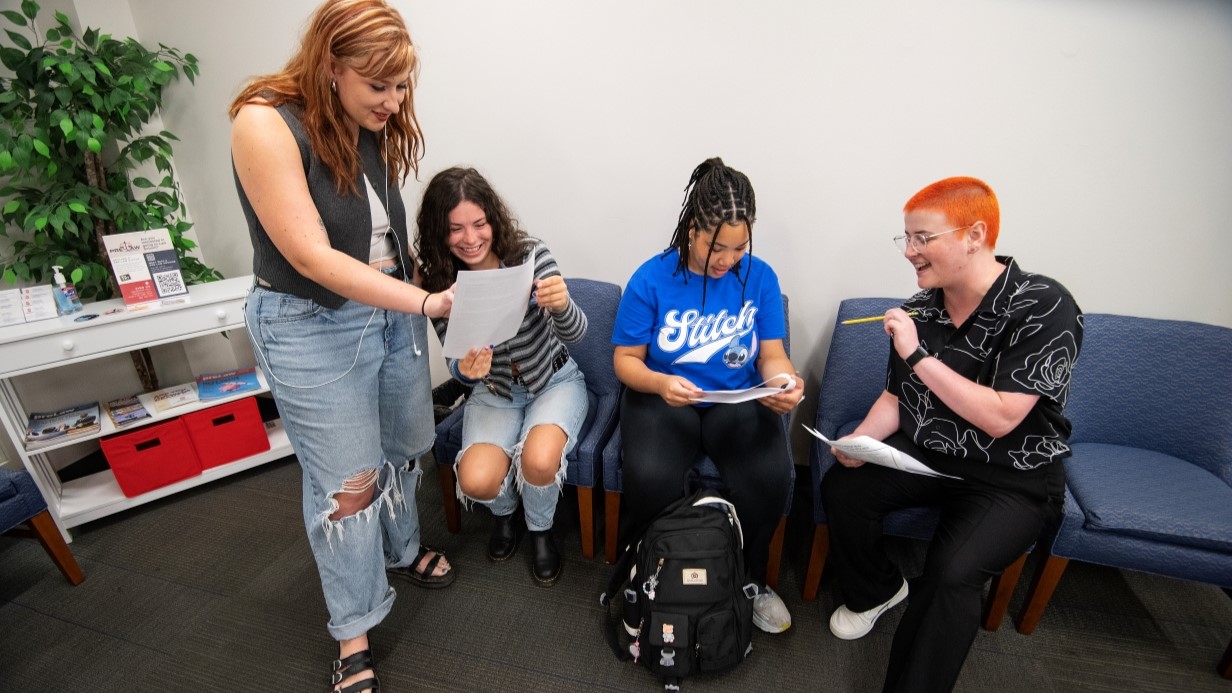 small group of students and an advisor talking together and looking at papers in the reception room of CLA student services