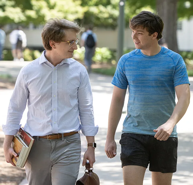 Professor and student walking and talking outside on a sunny day.