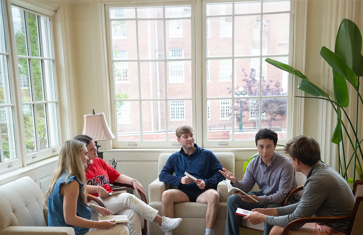 Group of three students and professor looking at open laptop computer