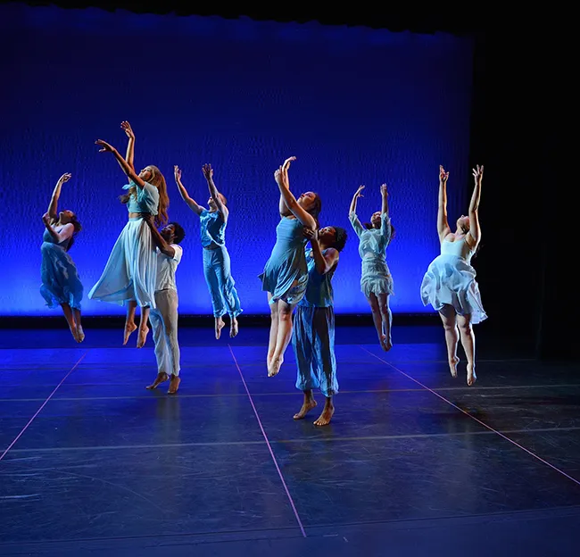 Dancers on stage leaping in the air lit by blue light