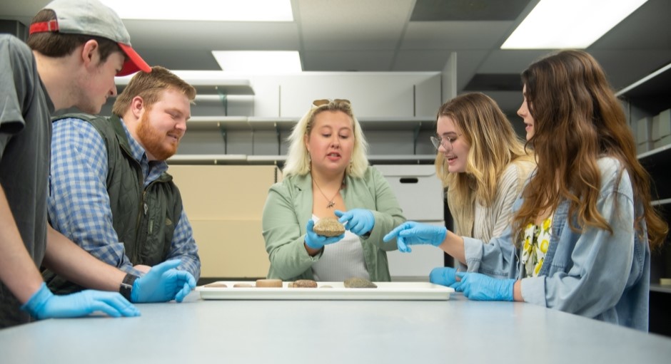 a group of anthropology students gathered around archaeology artifacts