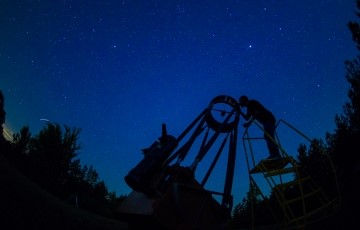 outline of a person looking through a telescope against the starry night sky