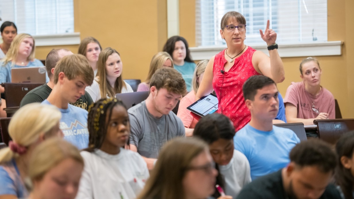 Professor in classroom talking to student seated at desk