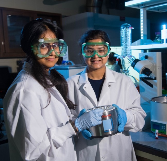 two chemistry students in eye goggles holding an instrument