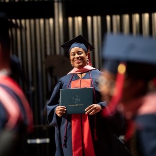 student in graduation robes holding her diploma cover