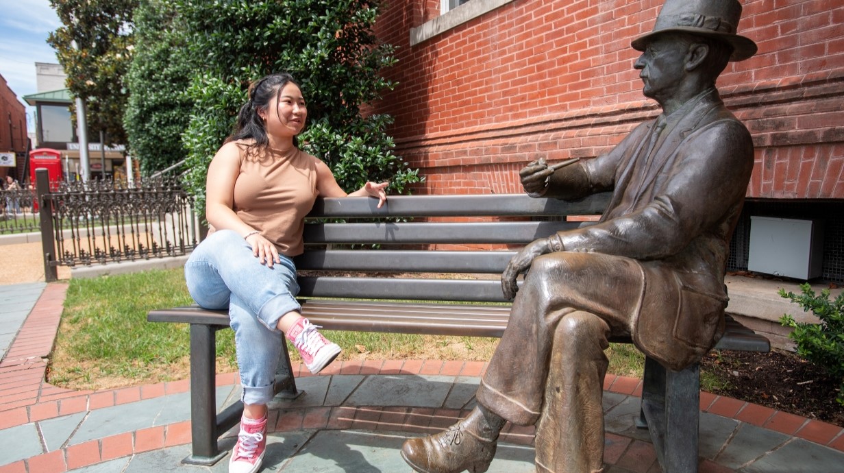 Student sitting on the bench with William Falkner statue