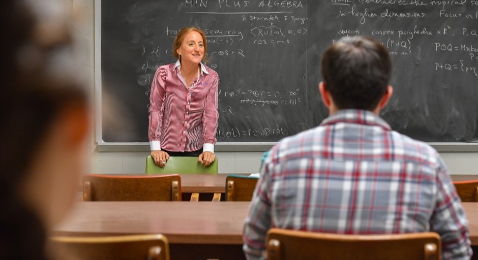 professor standing at the chalkboard smiling at the students in the class