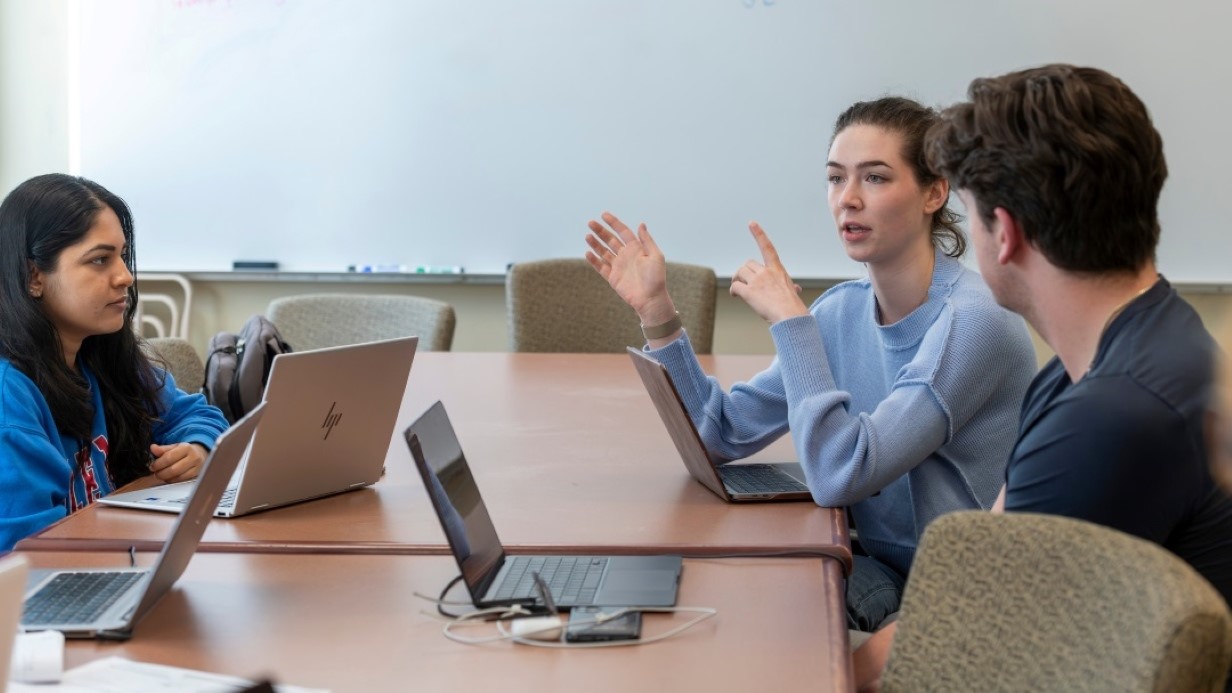 three students sitting around a table talking