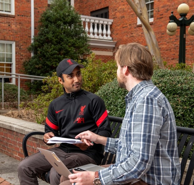 a faculty member and graduate student sitting together on a bench