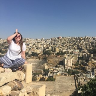 university student doing the land shark hand gesture while seated in front of a Middle Eastern town