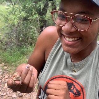 student standing outside holding a tiny frog for the camera