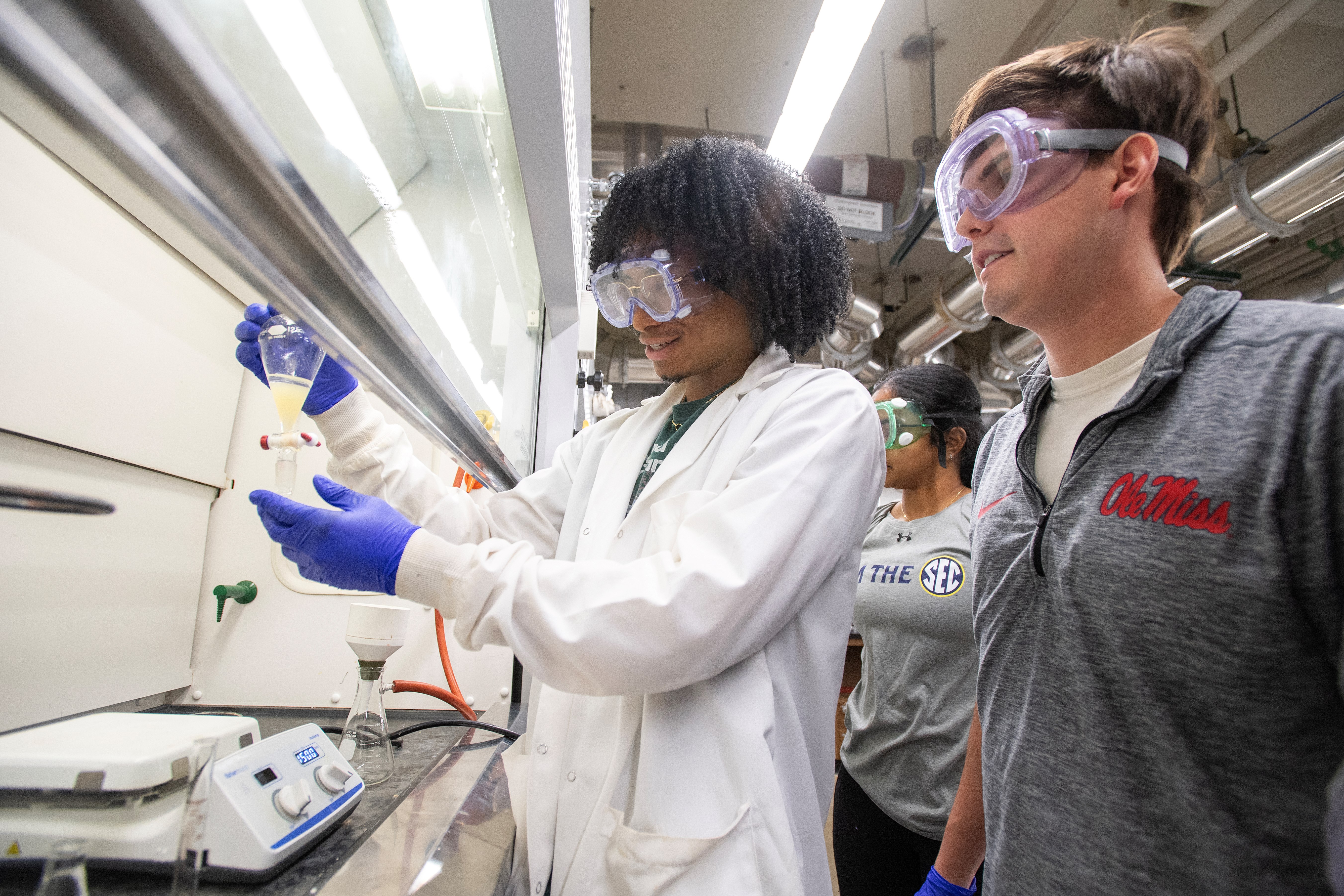 Two students conduct a chemistry experiment under a fume hood.