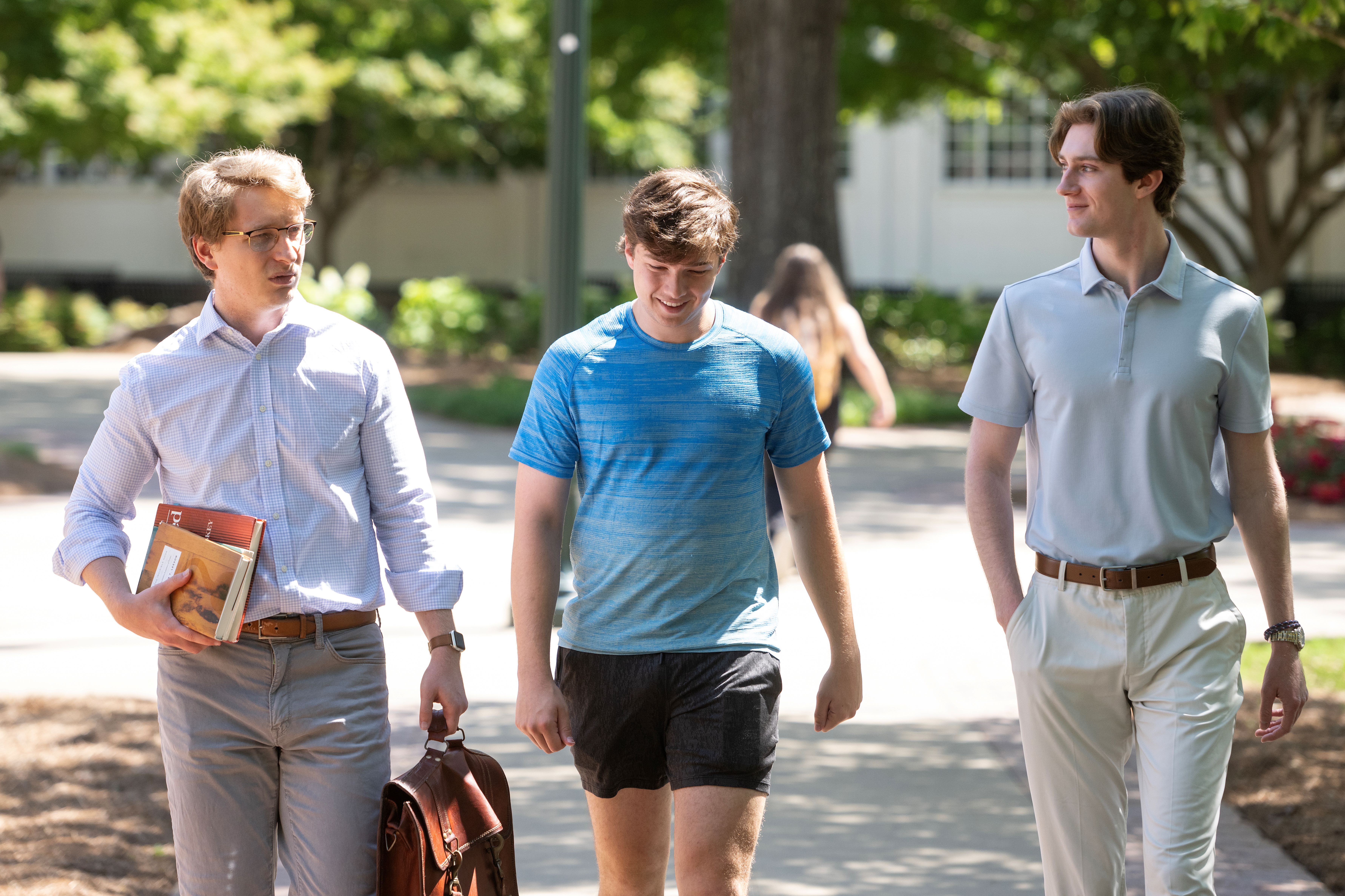 An economics professor walks and talks with two students.