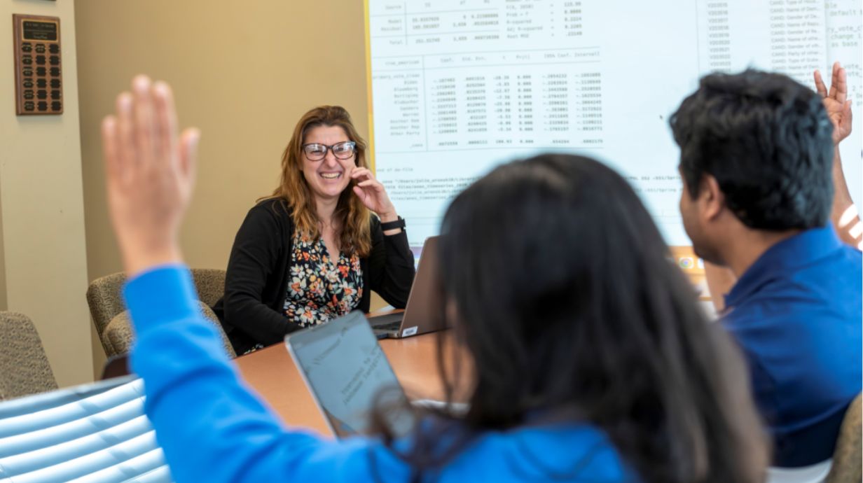 Professor smiling an gesturing at students around the table.