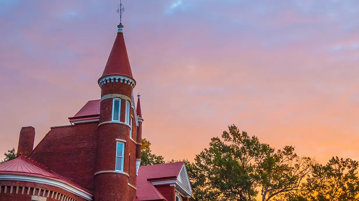 Image of Ventress Hall against the trees in the Grove with a pink sky at sunrise.