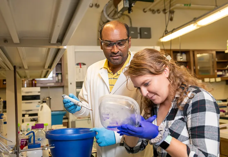 Professor and student working in a lab. Professor holds pipette and student holds specimen.