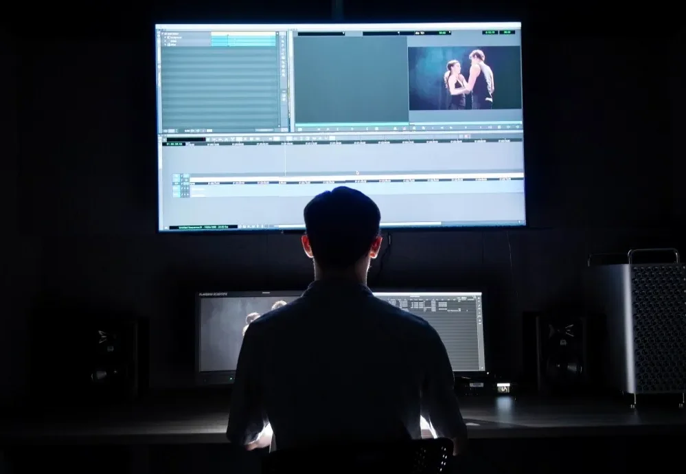 back of person in silhouette backlit by brightly lit computer monitors displaying video timeline 