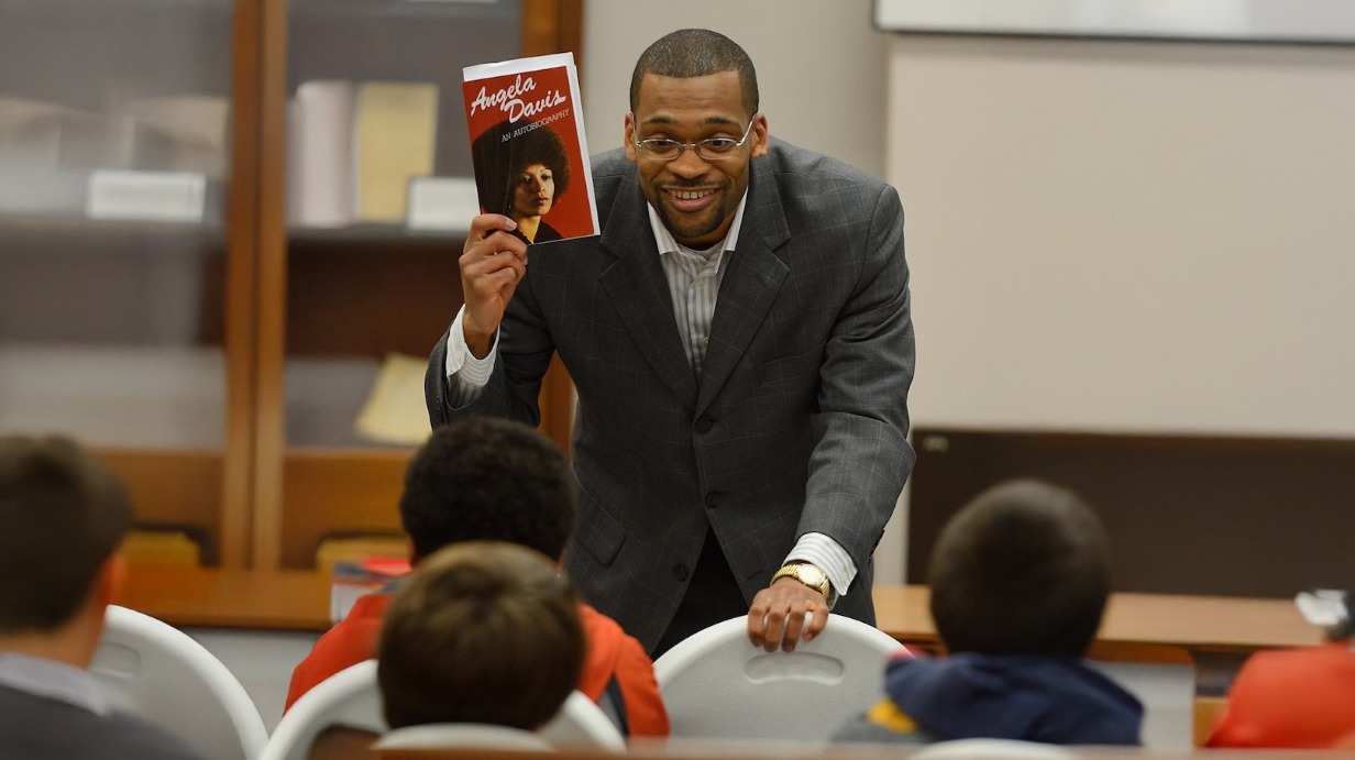 Dr. Patrick Alexander holding an Angela Davis book and smiling at an audience