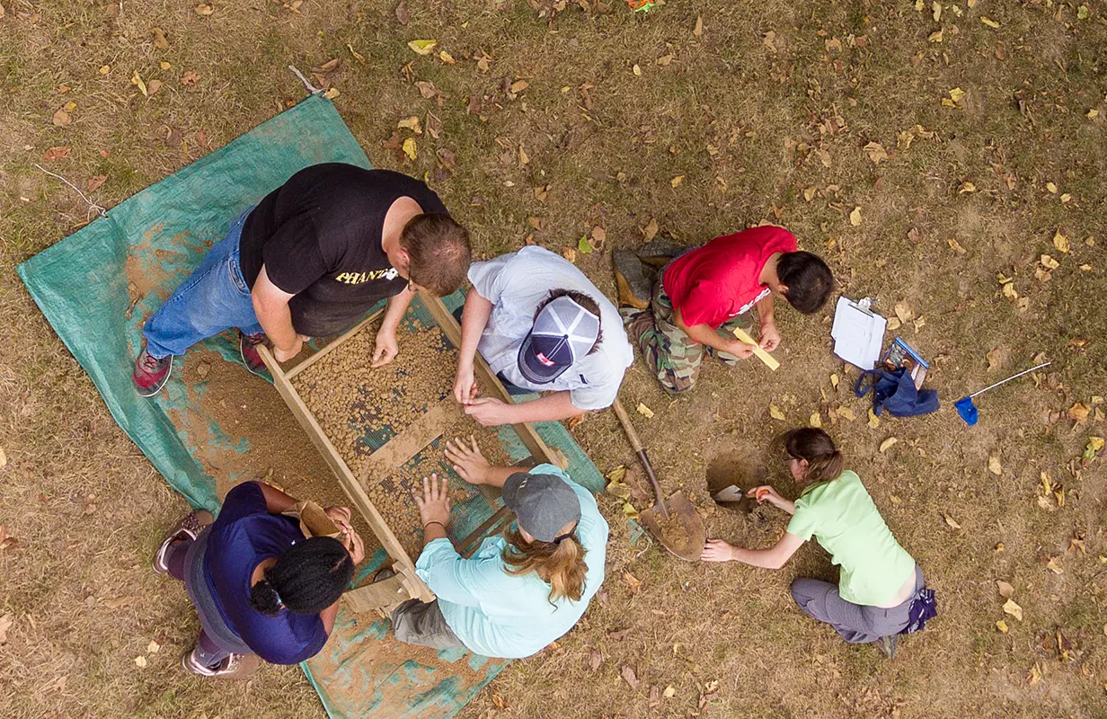 aerial image looking down at an archaeology field dig with people leaning over into the dig site