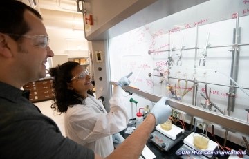 biochemistry graduate student standing at a vent hood with  professor and pointing at notes written on the glass