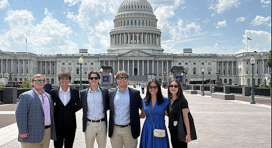Group of nine people standing in front of large ornate paintings and bronze scupltures.