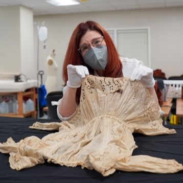 faculty member holding up historic children's clothing