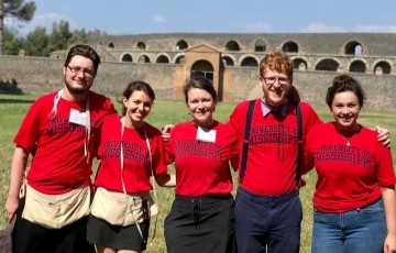 five people in bright red university of mississippi shirts standing together with ancient Italy ruins in the background