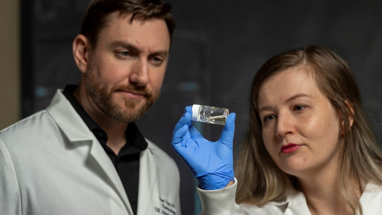 image of two faculty members looking at a glass vial of a clear liquid