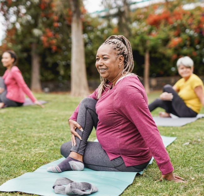 image of an older woman seated on a yoga mat doing a yoga pose outside on a grass lawn