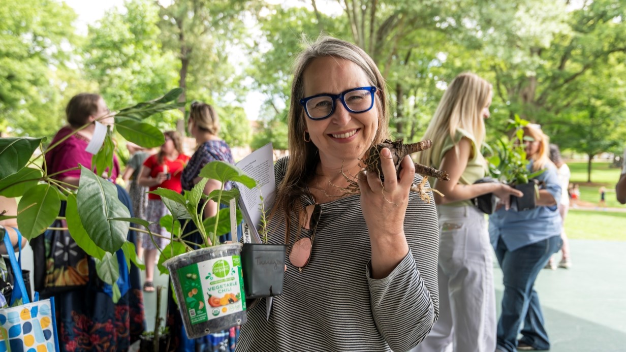 image of staff member smiling at the camera while holding a plant and a bulb at a Plant Swap event