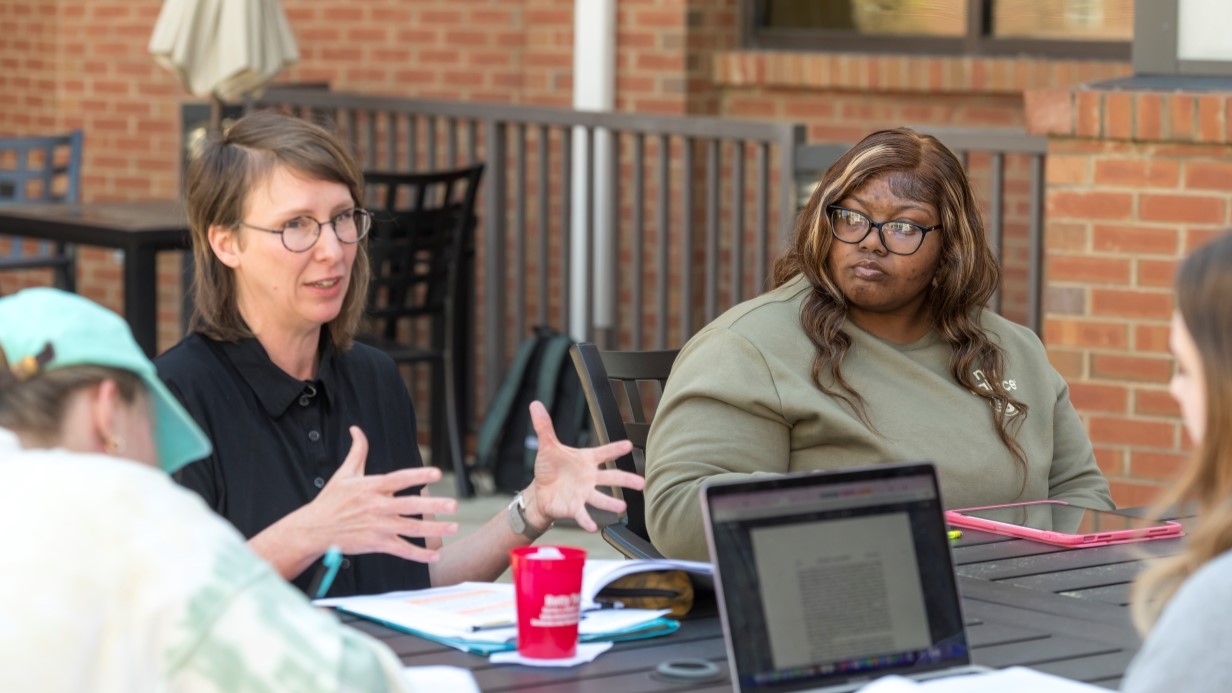 faculty member and students having class outside around a table