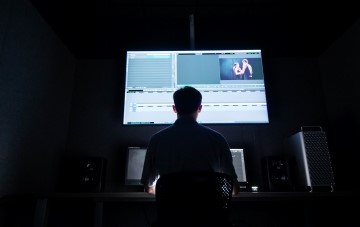 student sitting in a dark room with a large TV showing the editing process of a film project