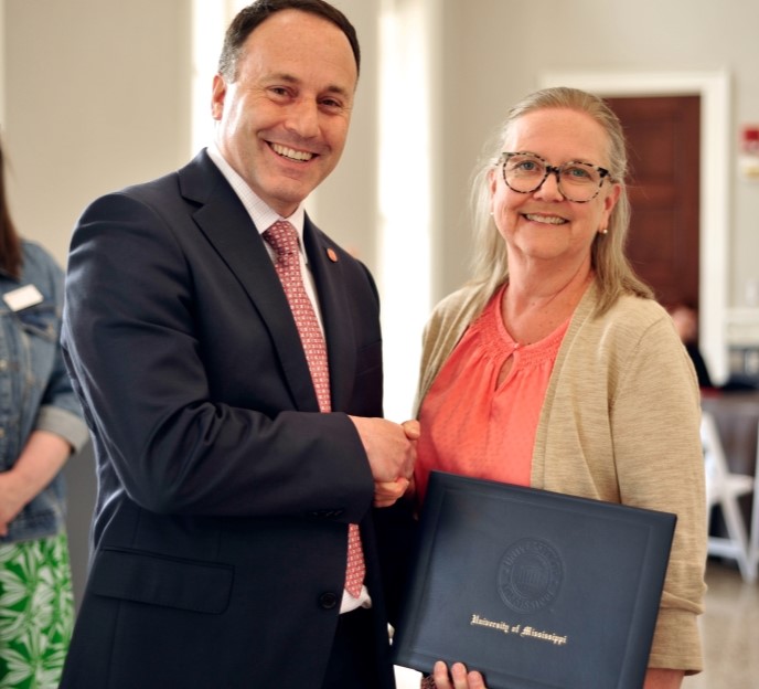 Dean is giving an award to a staff person. They are holding a diploma cover