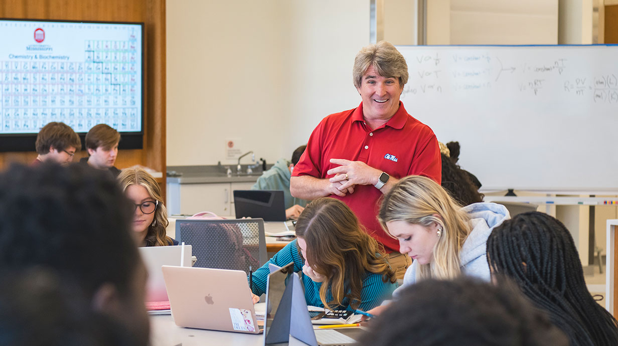 Professor in classroom talking to student seated at desk