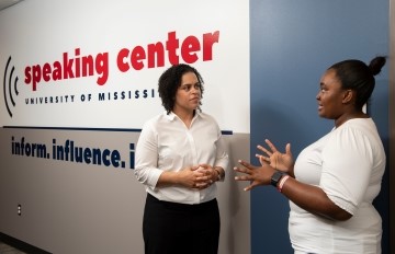 student and staff member standing in the hallway talking next to a sign for the Speaking Center