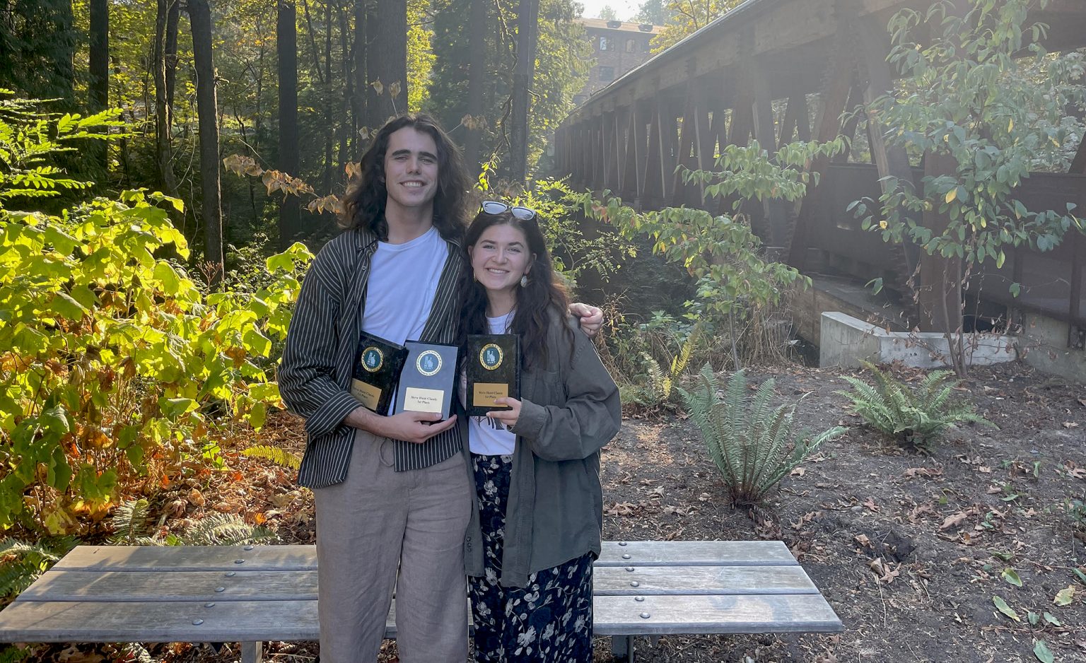 Two students standing outside holding award plaques