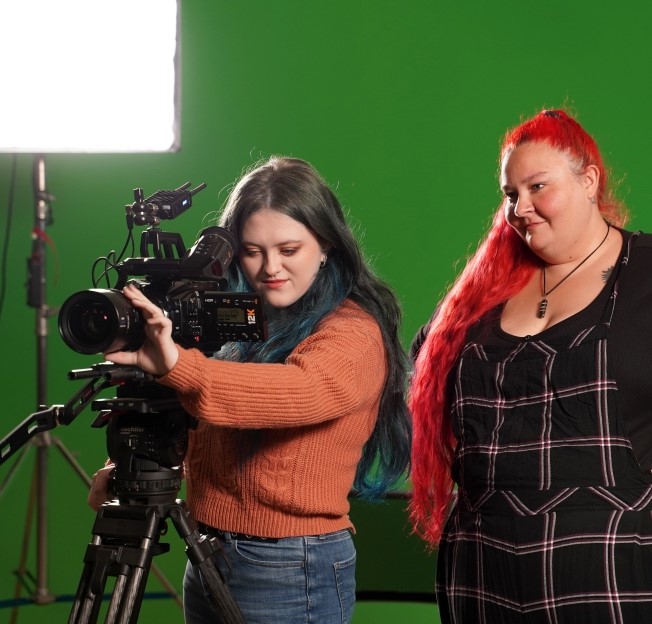 image of a student working a cinema camera while a faculty member looks over her shoulder