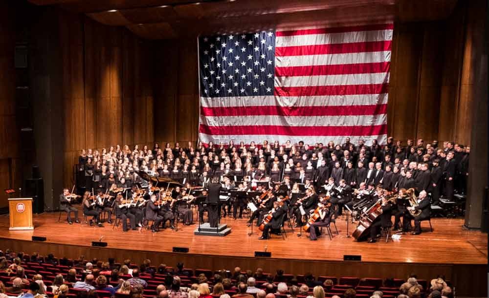 The UM Chorus performs in front of a large American flag.