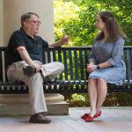 Dr. Dan O'Sullivan speaks with a student on a bench outside of Bondurant Hall.